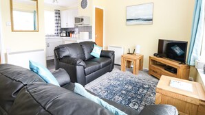 A living room with a black leather sofa, a wooden coffee table, and a television. - 20 Siesta Mar (Norwich)