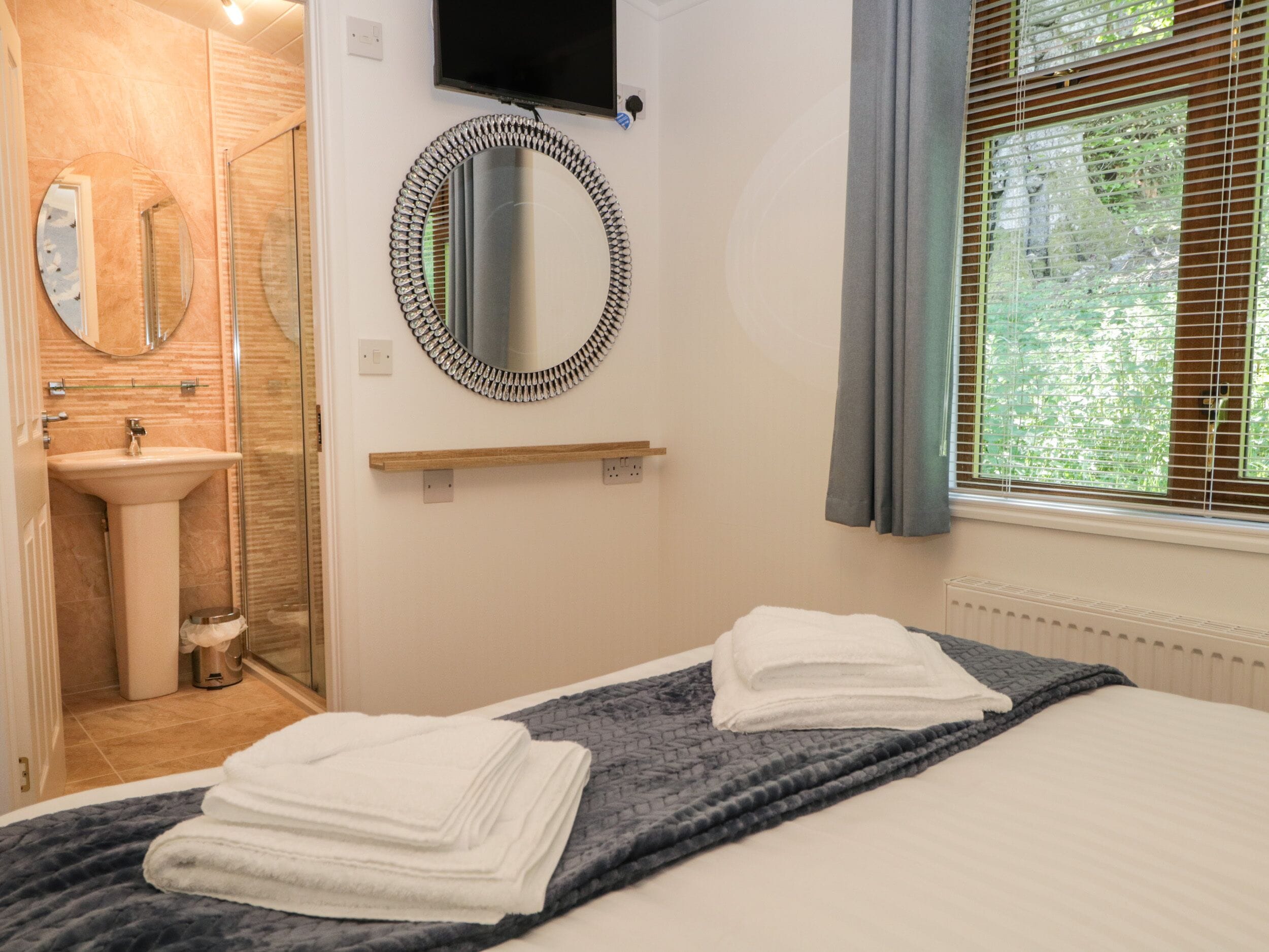 A hotel room with a bed, a bathroom with a sink, a mirror, and a television.