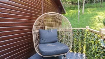 A wicker chair with a cushion on a wooden deck, adjacent to a wooden building with a sloped roof.