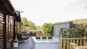 A wooden deck with a hot tub, wicker chairs, and a potted plant. - Broad Oak Lodge (Windermere)