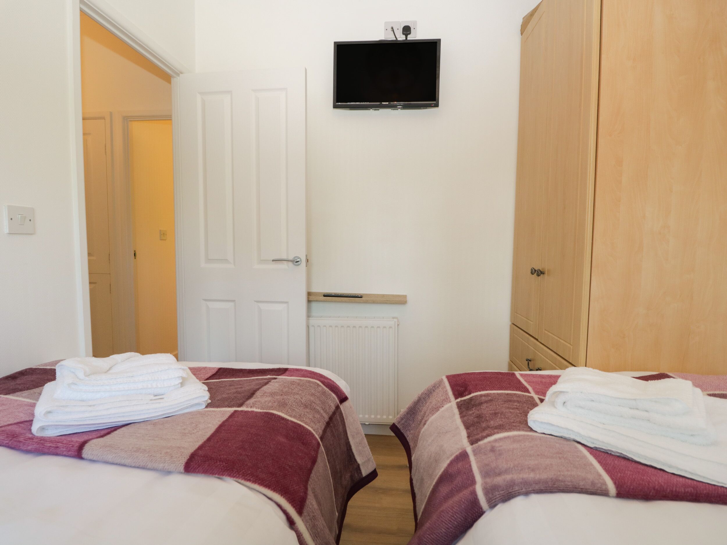 Habitación de hotel con dos camas, un televisor montado en la pared y un armario.