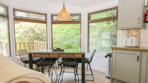 A modern kitchen with a dining area, large windows, and a view of greenery. - Broad Oak Lodge (Windermere)