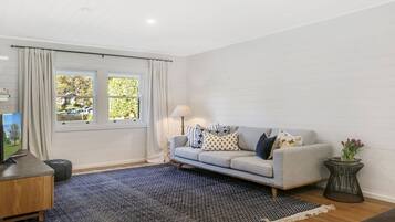 A living room with a grey sofa, a blue and black rug, a small side table, and a window with curtains.