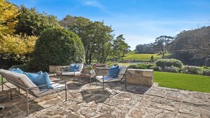 An outdoor patio with stone flooring, two lounge chairs with blue cushions, and a view of a lush garden and rolling hills in the background. - Protestant Hall - complete peace and tranquility (Wildes Meadow)