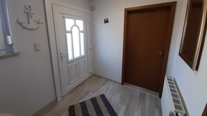 En gang med en trædør, en hvid dør med et vindue, en radiator og en stribet måtte.