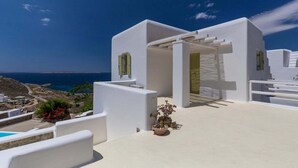 Un bâtiment blanc avec vue sur la mer, une piscine et des plantes en pot.