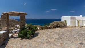 Un chemin de pierre mène à un bâtiment blanc surmonté d’une arche en pierre, d’où l’on peut admirer une vue sur la côte.