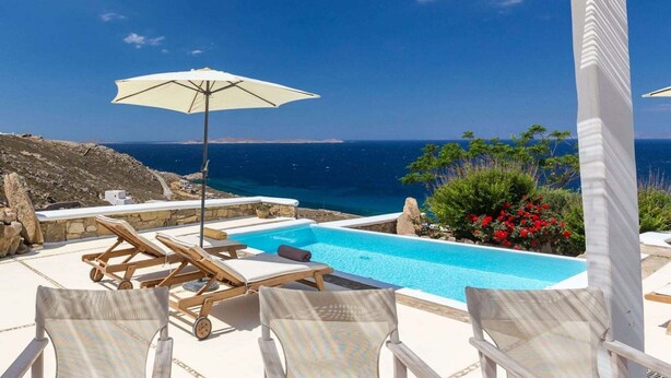 Une piscine dotée de chaises longues et d’un parasol, offrant une vue dégagée sur la côte et la mer.