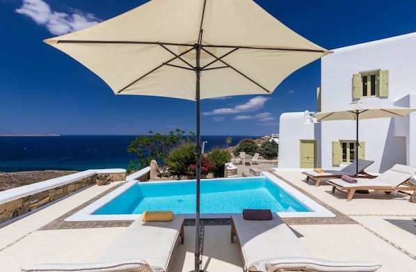 Relax by the serene pool overlooking the ocean, surrounded by lounge chairs and umbrellas.