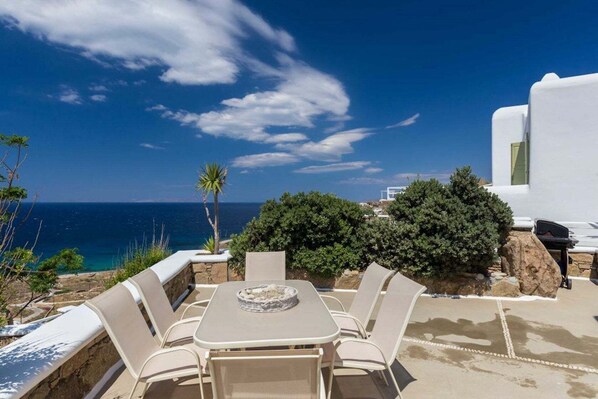 An outdoor dining area with a table and chairs, overlooking the sea.