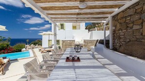 Un espace extérieur ensoleillé, aménagé avec des sièges, une piscine, des murs en pierre et une vue sur la mer.