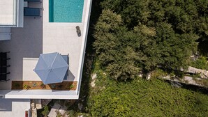 Ovenudblik over en moderne bygning med swimmingpool, udendørs siddepladser og en have.