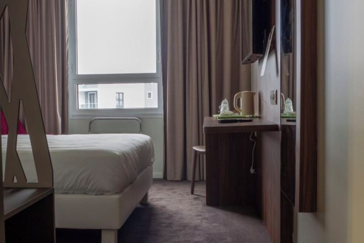 Une chambre d’hôtel avec un lit, un bureau et une fenêtre avec des rideaux.
