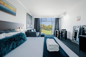 A hotel room with a large bed, a sofa, a dining table with chairs, and a view of a golf course.
