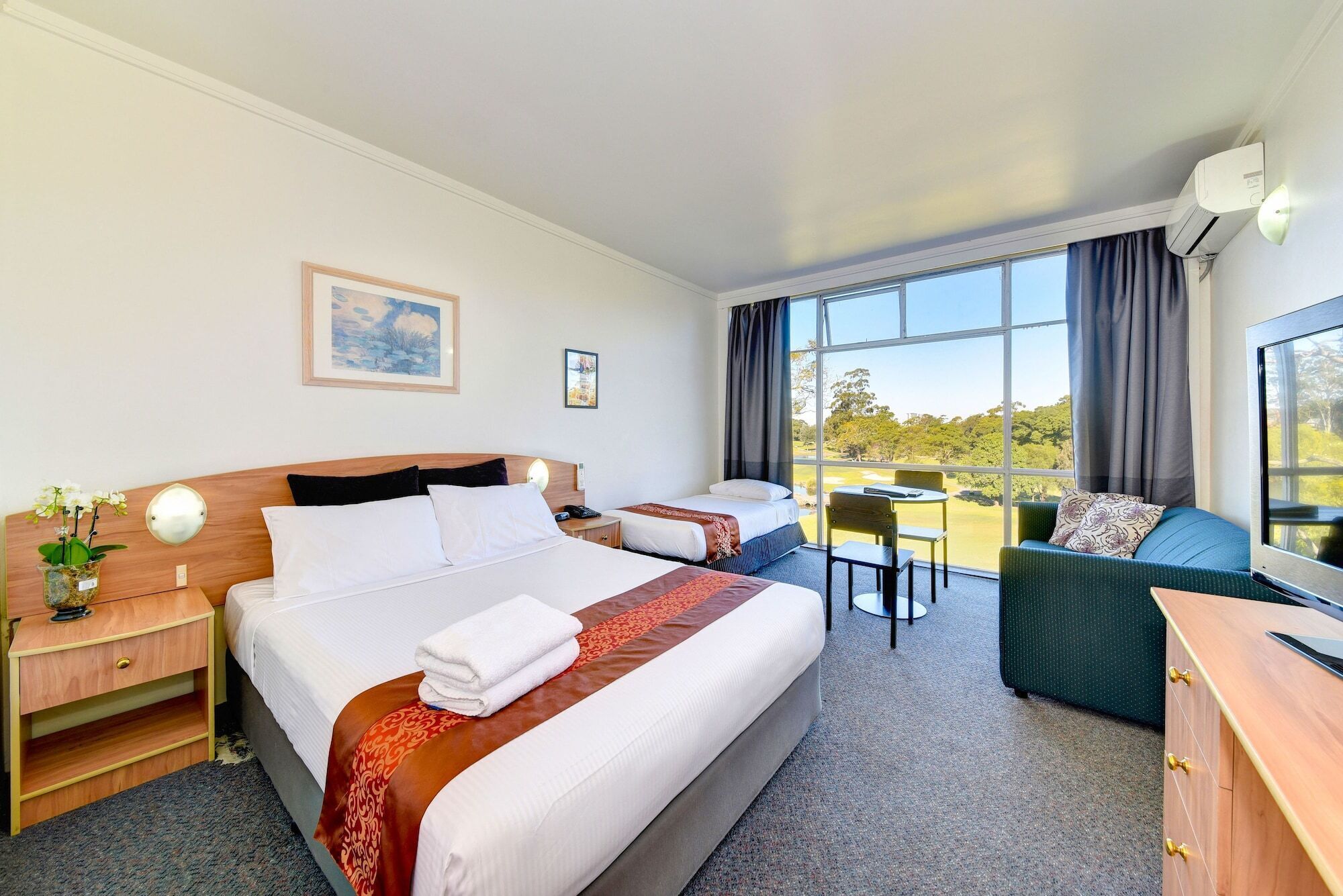 A hotel room with two beds, a desk, a chair, and a large window offering a view of the outdoors.