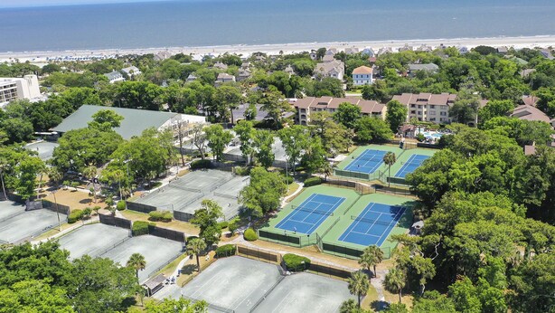 Vista aérea de una zona residencial con múltiples canchas de tenis, una playa y una gran masa de agua al fondo.