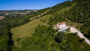 A two-story house with a swimming pool surrounded by lush greenery and hills in the background.