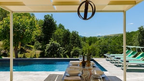 A poolside dining area with a view of a lush green landscape and hills.