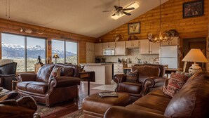 Un salón amplio con sofás de cuero y un ventanal con vistas a un paisaje montañoso.