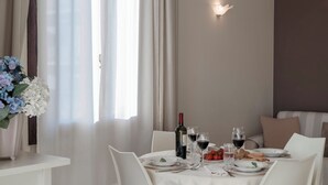 A dining area with a table set for four, including wine glasses, a bottle of wine, and plates with food. - Arcimboldo House 2+2, Emma Villas (Sirmione)
