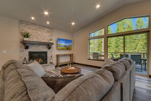 A spacious living room with a stone fireplace, a large window offering a view of trees, and a cozy seating area.