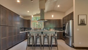 A modern kitchen with dark wood cabinets, a central island with bar stools, stainless steel appliances, and pendant lighting. - Built in 2021, Chef's Kitchen, Classic Arcade, 200mbps Wifi, Grill, Close to Heavenly: North Woods (South Lake Tahoe)