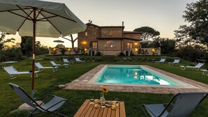 Ein Poolbereich mit Liegestühlen, einem Holztisch mit Gläsern und einem Haus im Hintergrund.