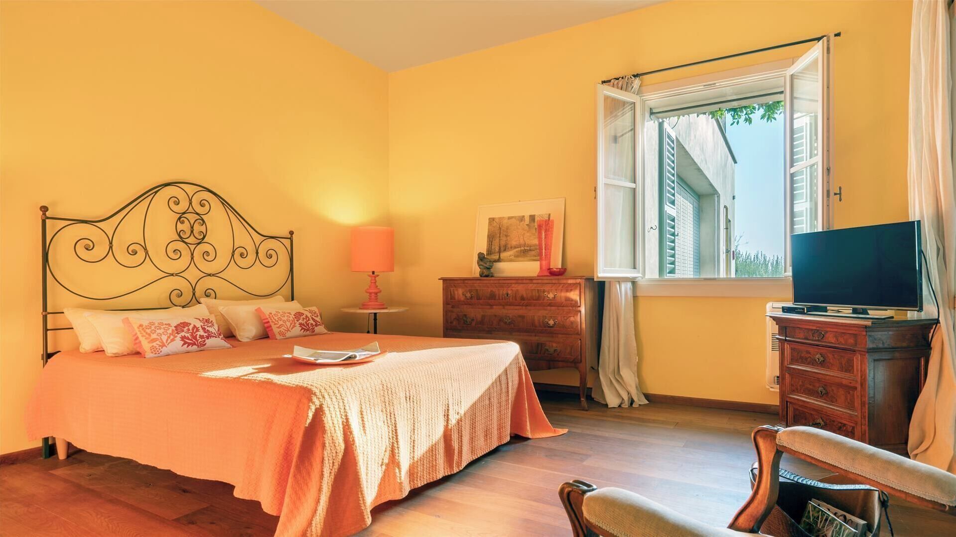 A bedroom with a bed, a dresser, a television, and a window with curtains.