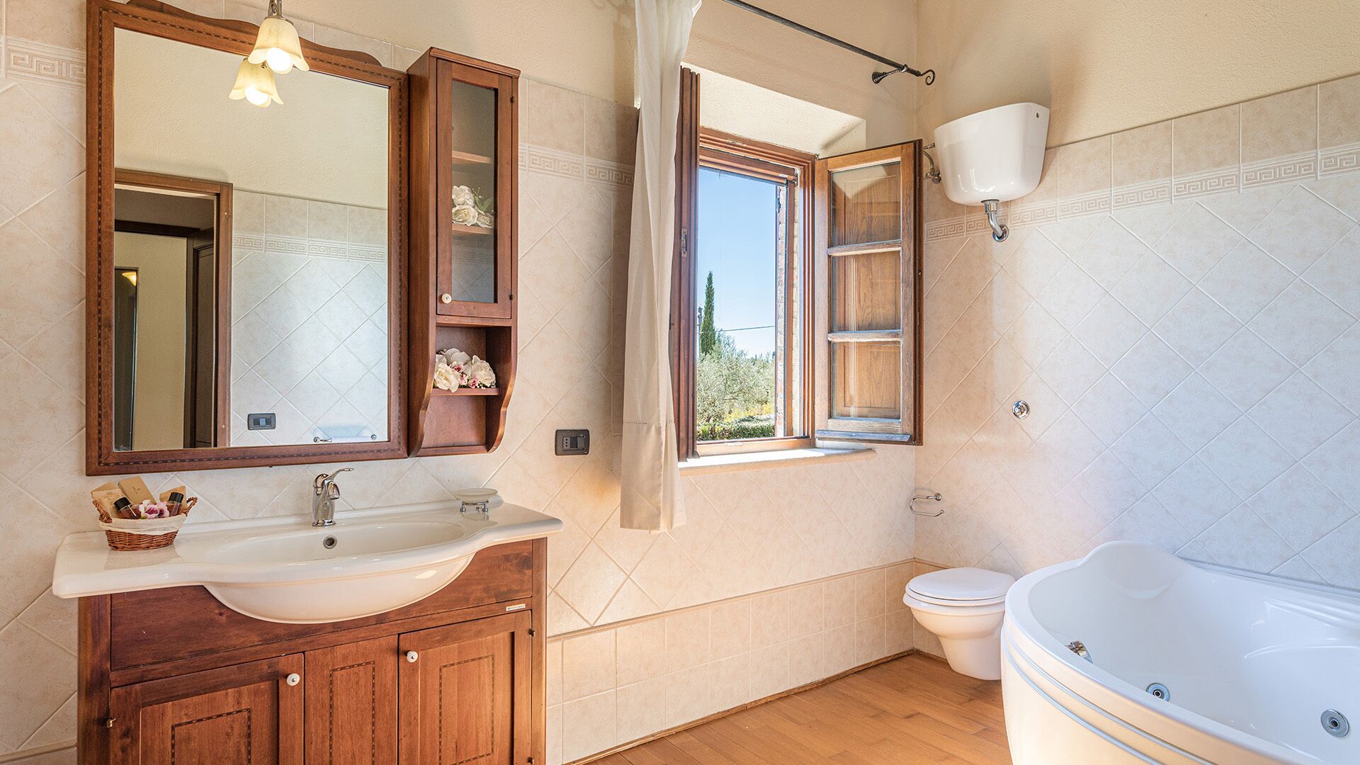 Een badkamer met een houten wastafelmeubel, een grote spiegel, een raam met uitzicht, een toilet en een bad.
