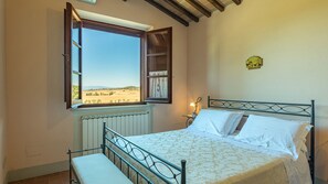 A bedroom with a bed, a window with an open shutter, a radiator, and a wall-mounted clock. - Il Fitto 10, Emma Villas (Cortona)