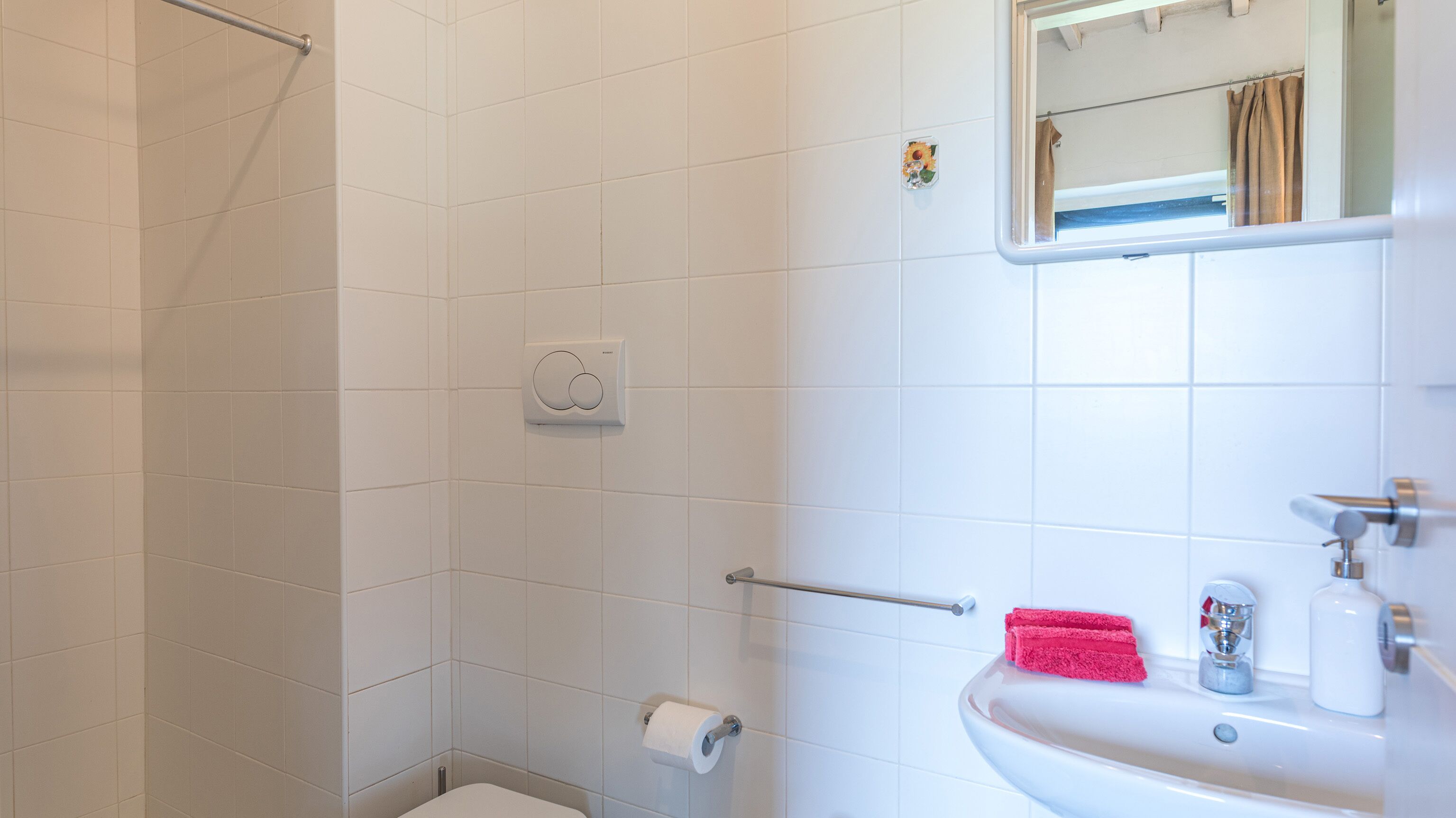A bathroom with white tiles, a toilet, a sink, a mirror, and a towel rack.