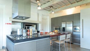 A modern kitchen with stainless steel appliances, a central island with bar stools, and pendant lighting. - Villa Le Fontane 12, Emma Villas (Todi)