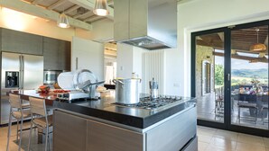 A modern kitchen with stainless steel appliances, a built-in stove, and a large island with bar stools. - Villa Le Fontane 12, Emma Villas (Todi)