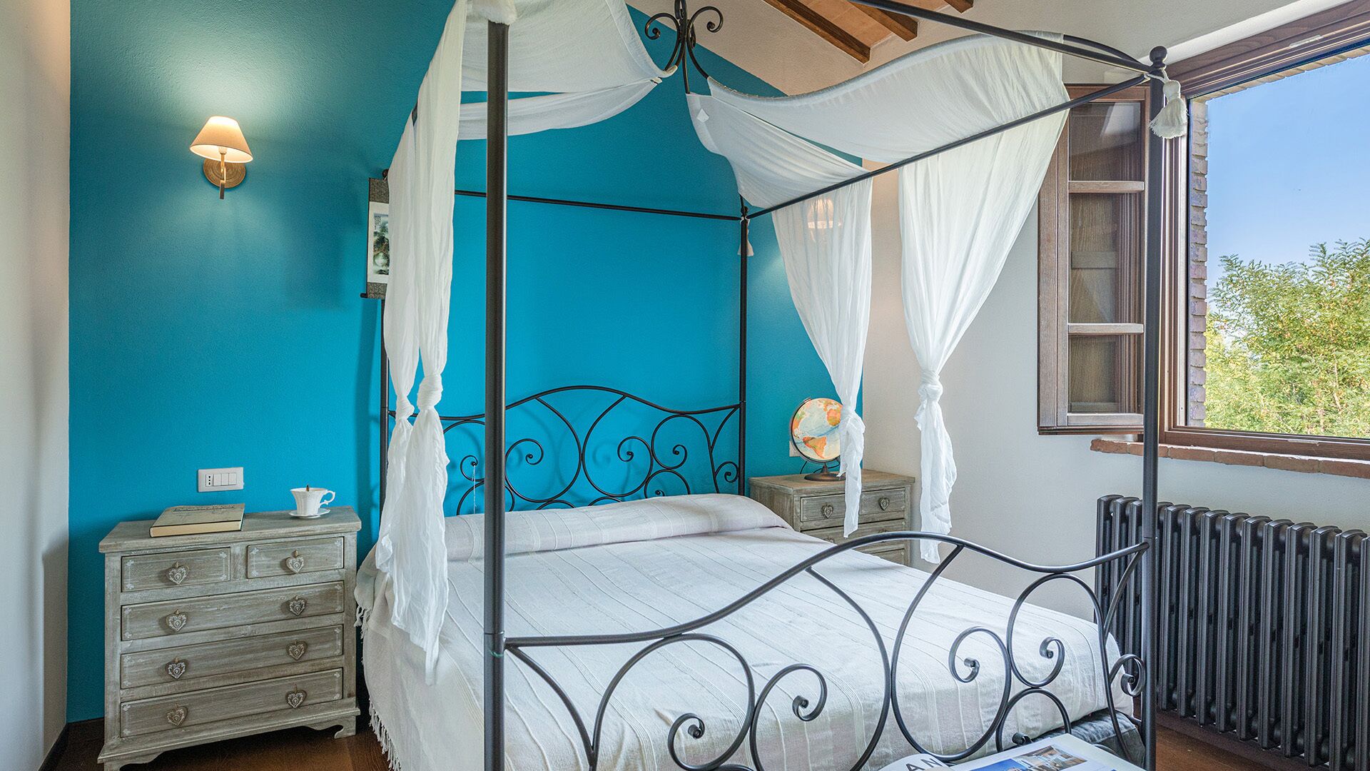 A four-poster bed with a canopy, a bedside table with a lamp, and a dresser with drawers.