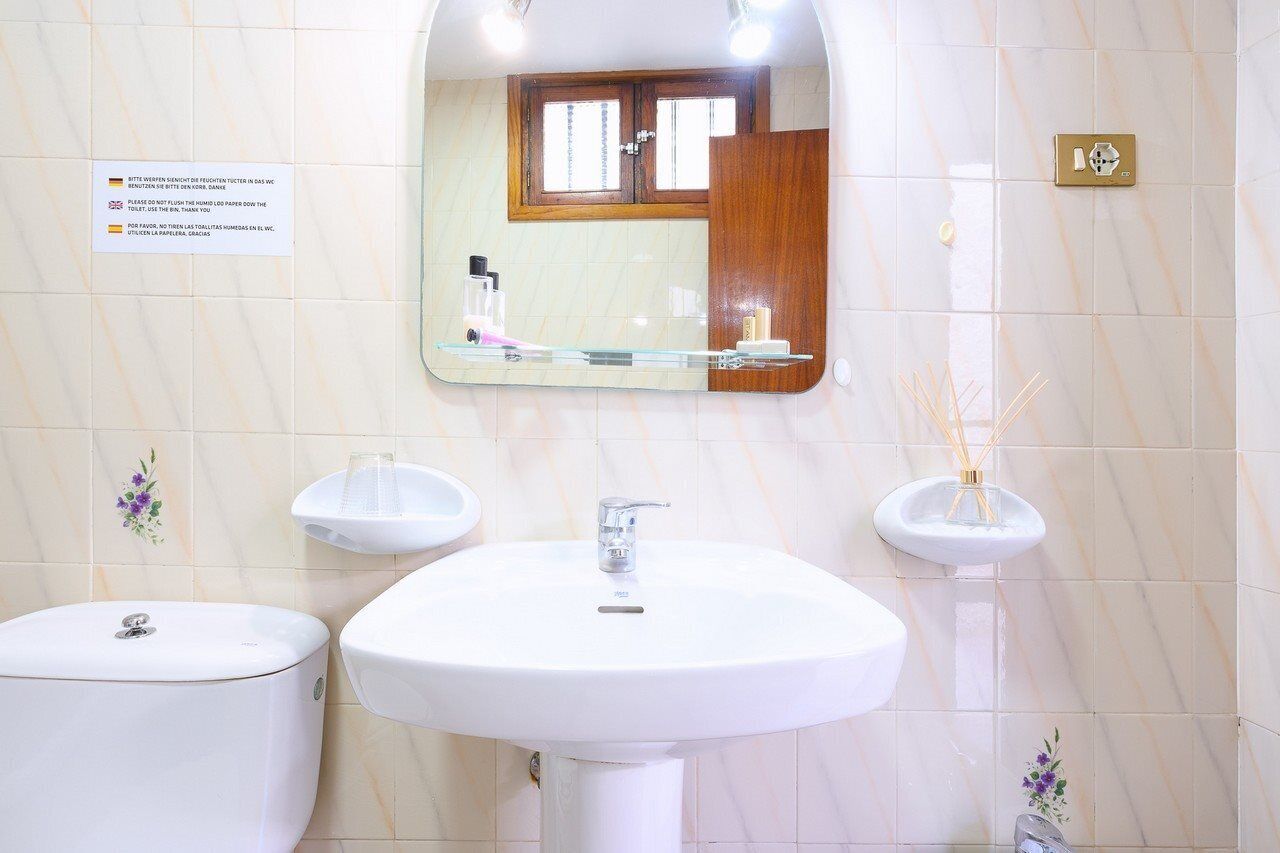 A bathroom with a white sink, a toilet, and a mirror. There is a sign on the wall and a small window above the mirror.