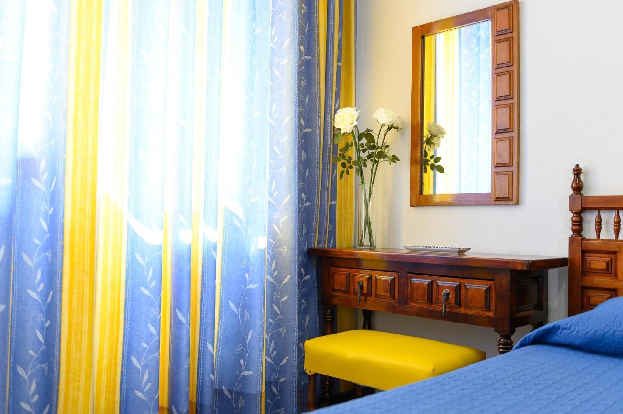 A room with a bed, a wooden dresser, a mirror, and a vase with flowers.