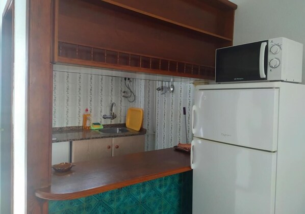 A compact kitchen with a microwave on top of a white refrigerator, a wooden countertop, and a sink with a yellow dish.
