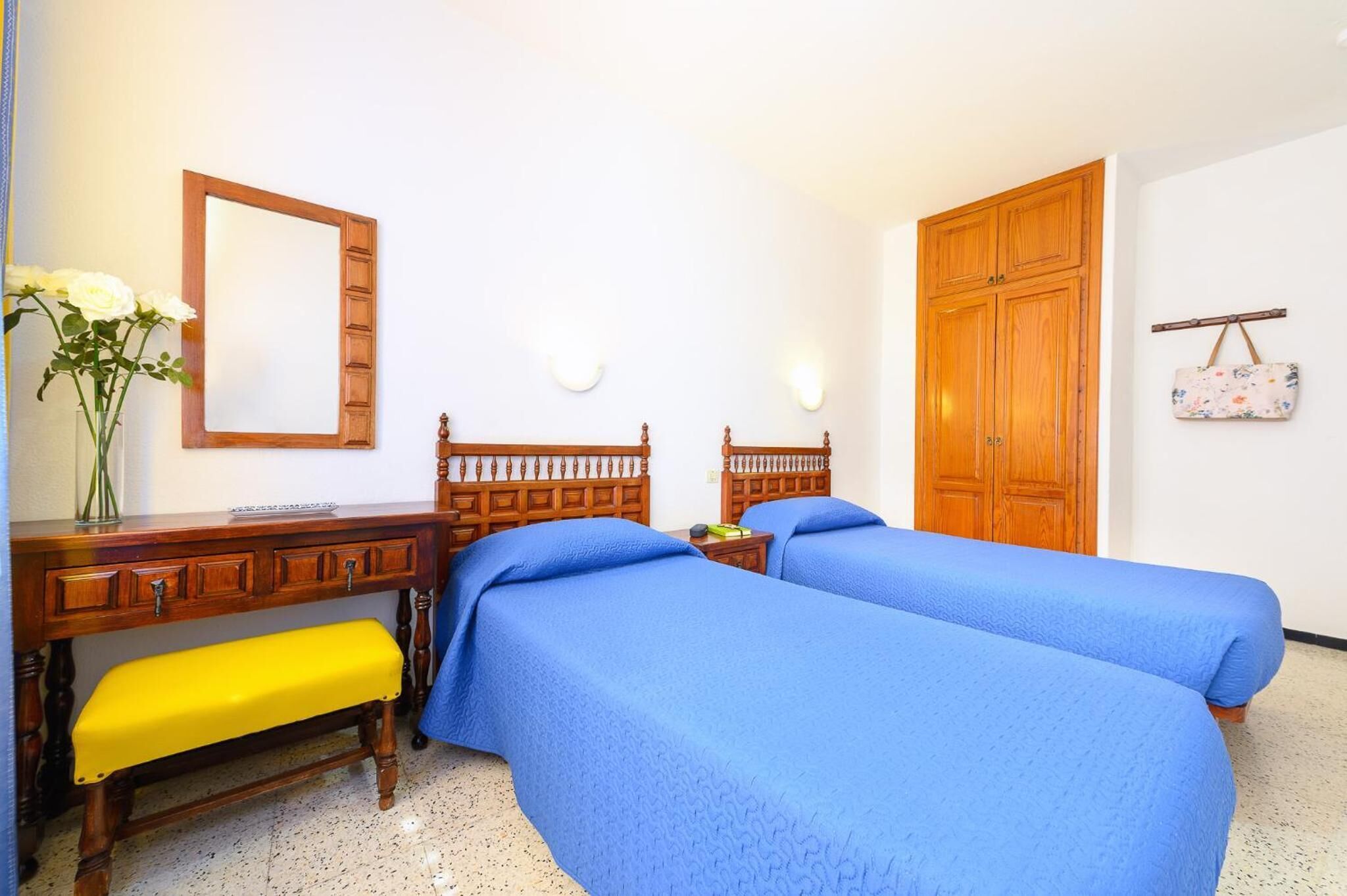 A room with two beds, a wooden desk, a bench, a mirror, and a wardrobe.