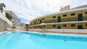 Una piscina con sillas de descanso y sombrillas, rodeada de edificios con balcones y ventanas.