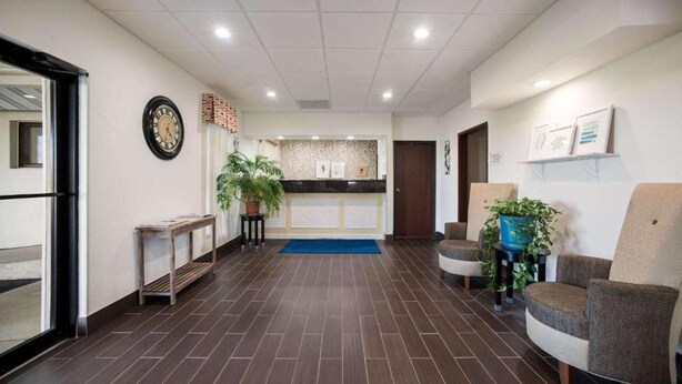 A reception area with a reception desk, a clock, and potted plants. - Ramada by Wyndham Effingham (Effingham)