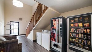 A hotel room with a sofa, a refrigerator, a vending machine, a staircase, and a laundry area. - Ramada by Wyndham Effingham (Effingham)