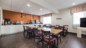A dining area with a large wooden table surrounded by chairs, a kitchen area with appliances, and a television on a stand. - Ramada by Wyndham Effingham (Effingham)