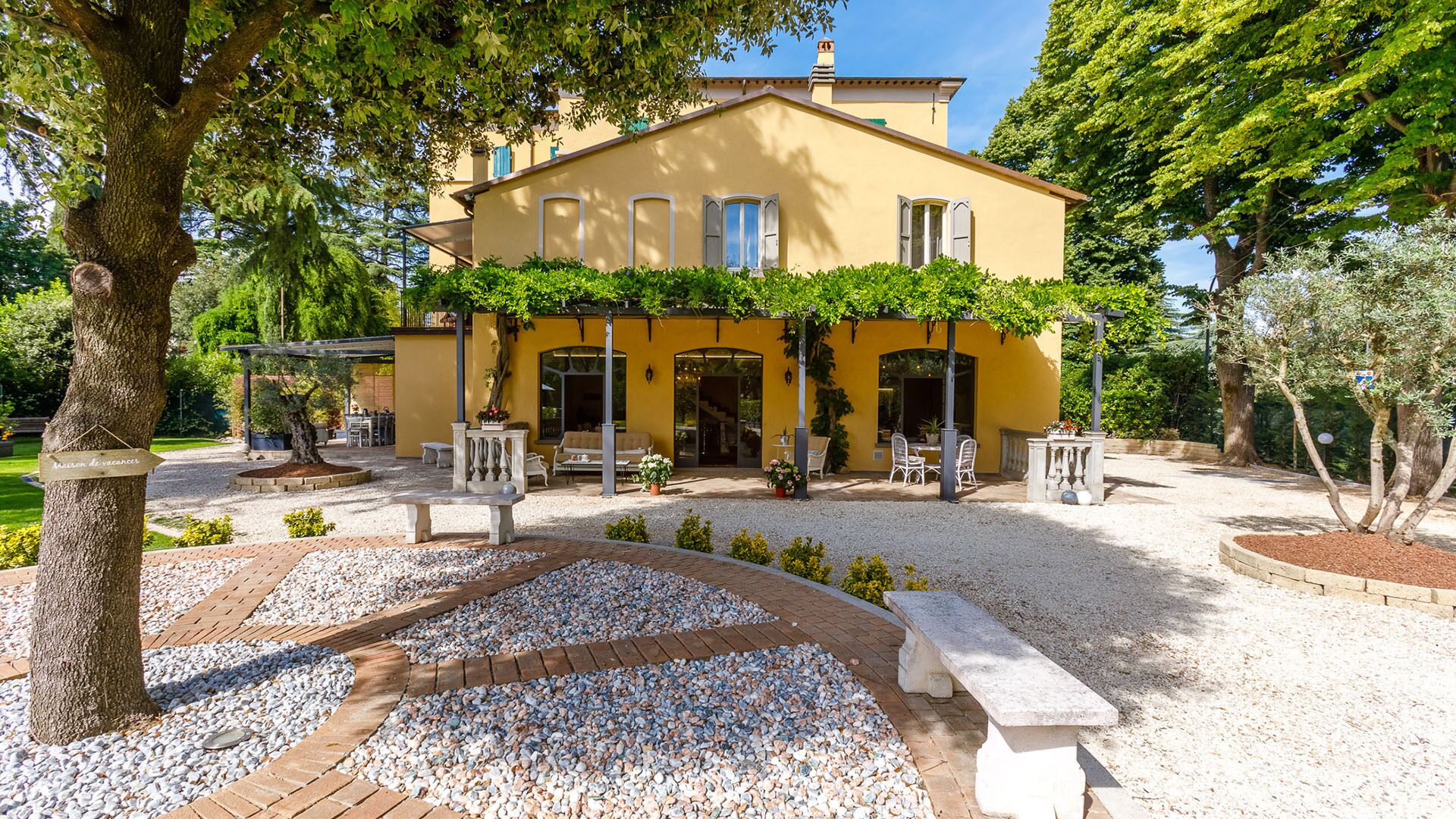 Una villa amarilla con patio, mobiliario exterior y un camino de grava.
