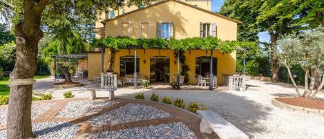 Una villa amarilla con patio, mobiliario exterior y un camino de grava.
