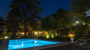 A swimming pool at night with surrounding trees and a building with illuminated windows. - La Casa Di Nanì 8, Emma Villas (San Lorenzo In Noceto)