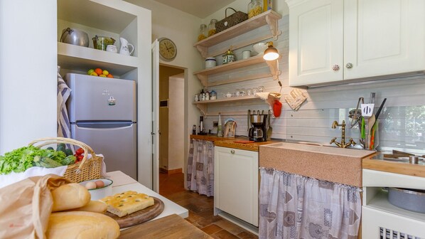 A compact kitchen with a refrigerator, shelves with jars and kitchenware, a coffee maker, and a sink with utensils. - La Casa Di Nanì 8, Emma Villas (San Lorenzo In Noceto)