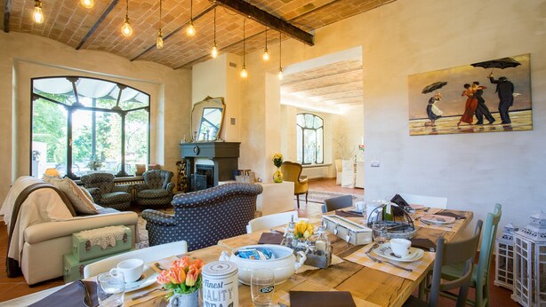 A spacious living room with a fireplace, comfortable seating, a dining area with a table set for two, and large windows offering a view of the outdoors. - La Casa Di Nanì 8, Emma Villas (San Lorenzo In Noceto)