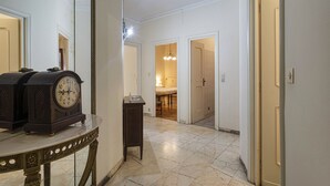 A hallway with a marble floor, a grandfather clock, and a mirror.