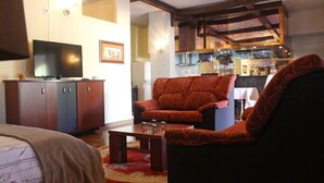 Una sala de estar con sofá, televisor, mesa de centro y una cocina al fondo.