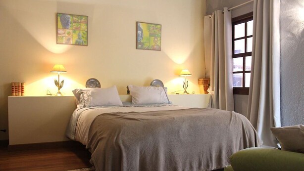 Un dormitorio con una cama, dos lámparas de noche, una ventana con cortinas y dos cuadros en la pared.